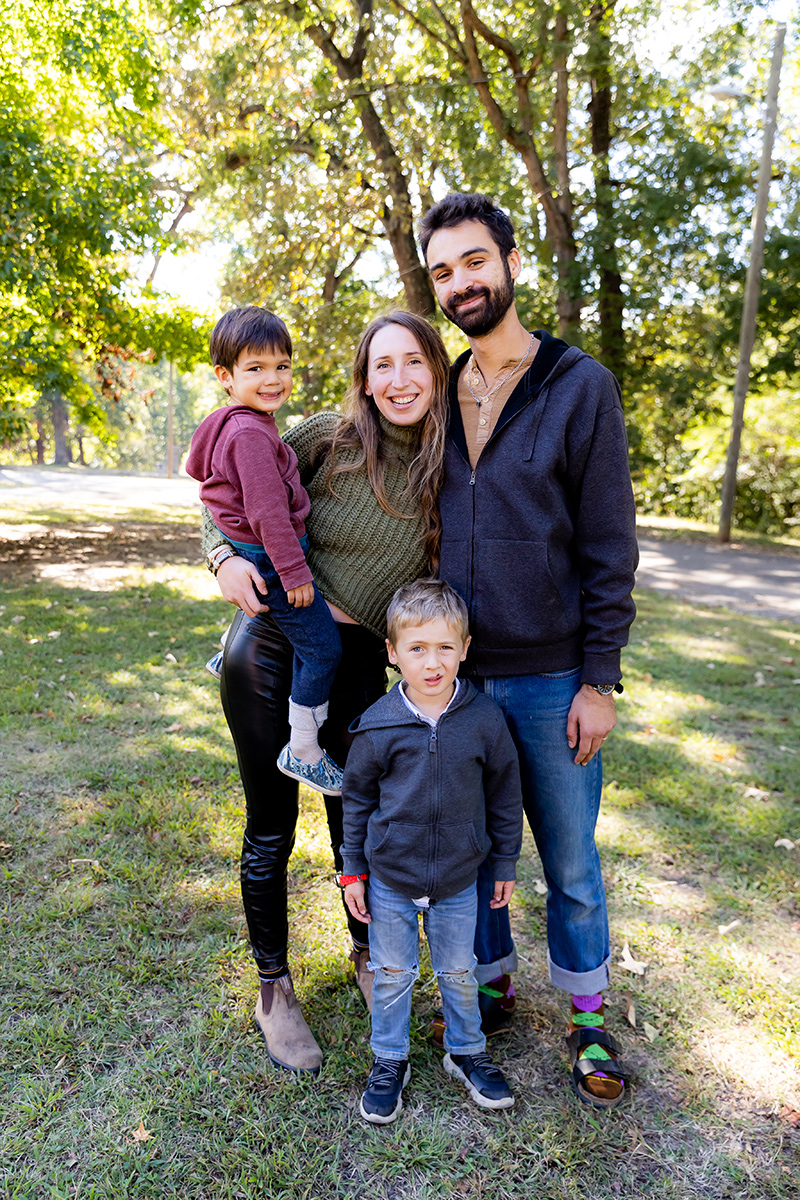 mwclt-family-outdoors Family of four, mom, dad, two sons stands outside in a park setting